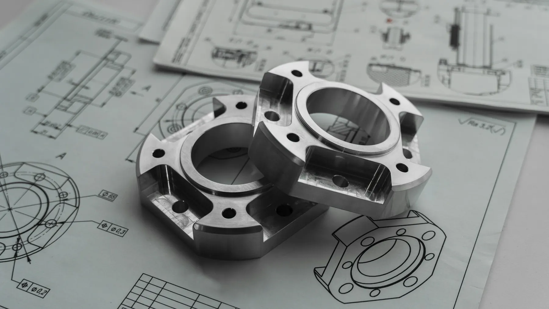 Machined steel parts resting on engineering drawings